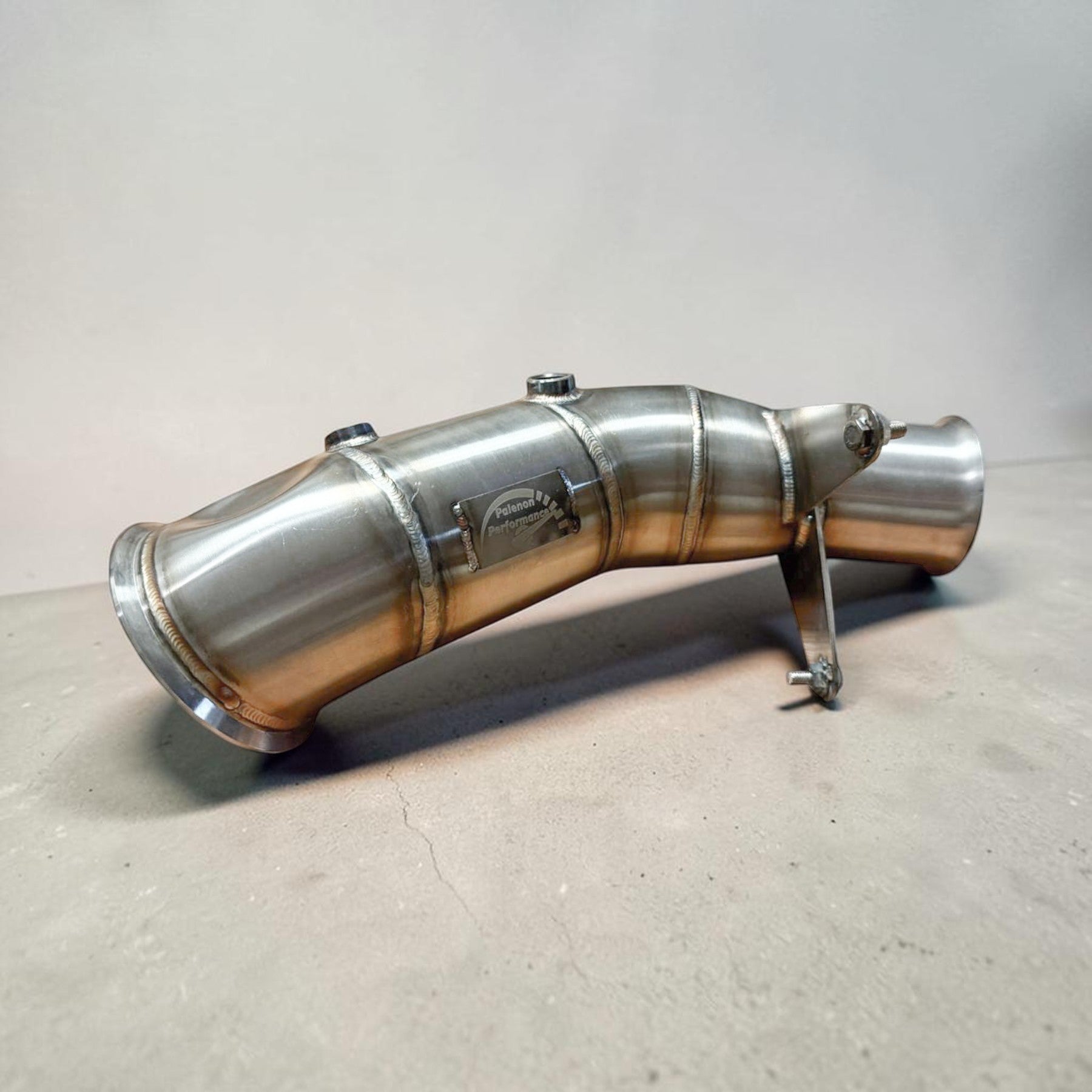 Metallic BMW N55 exhaust pipe on a gray surface with a neutral background