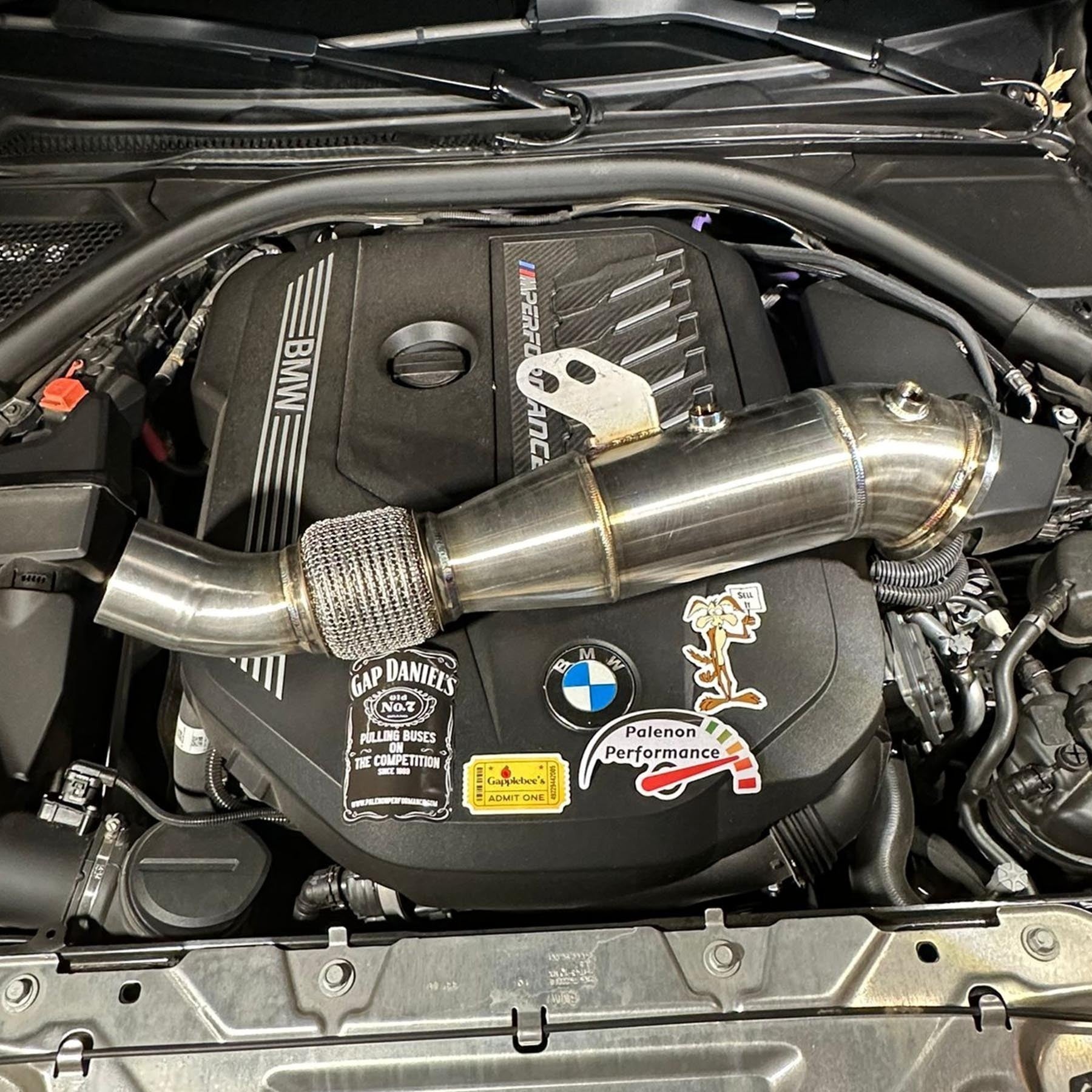 Palenon Performance 4.5-inch stainless steel racing downpipe resting on a BMW B58 engine bay