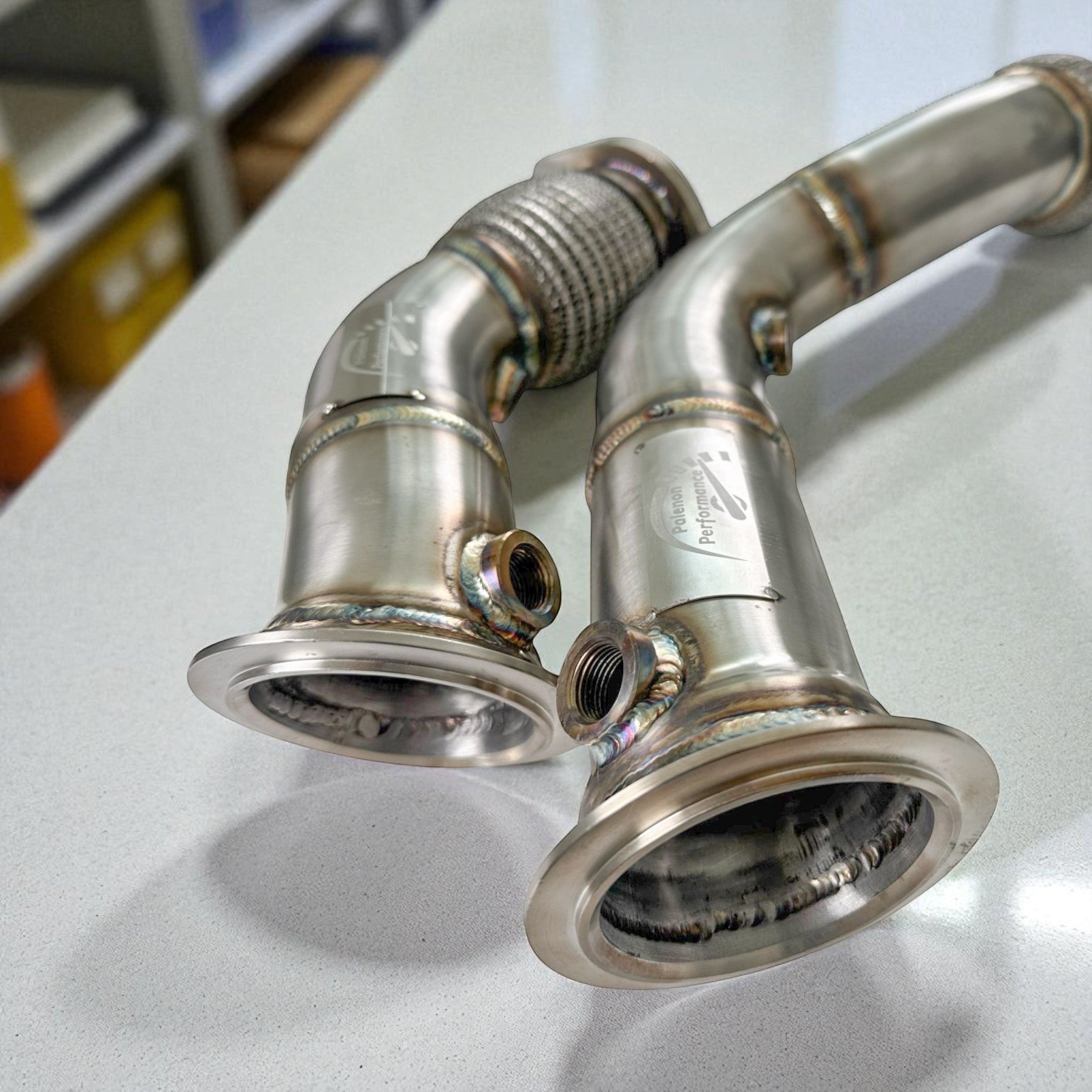 Palenon Performance stainless steel racing downpipes for BMW S55 engines featuring precision welds and V-band flanges.