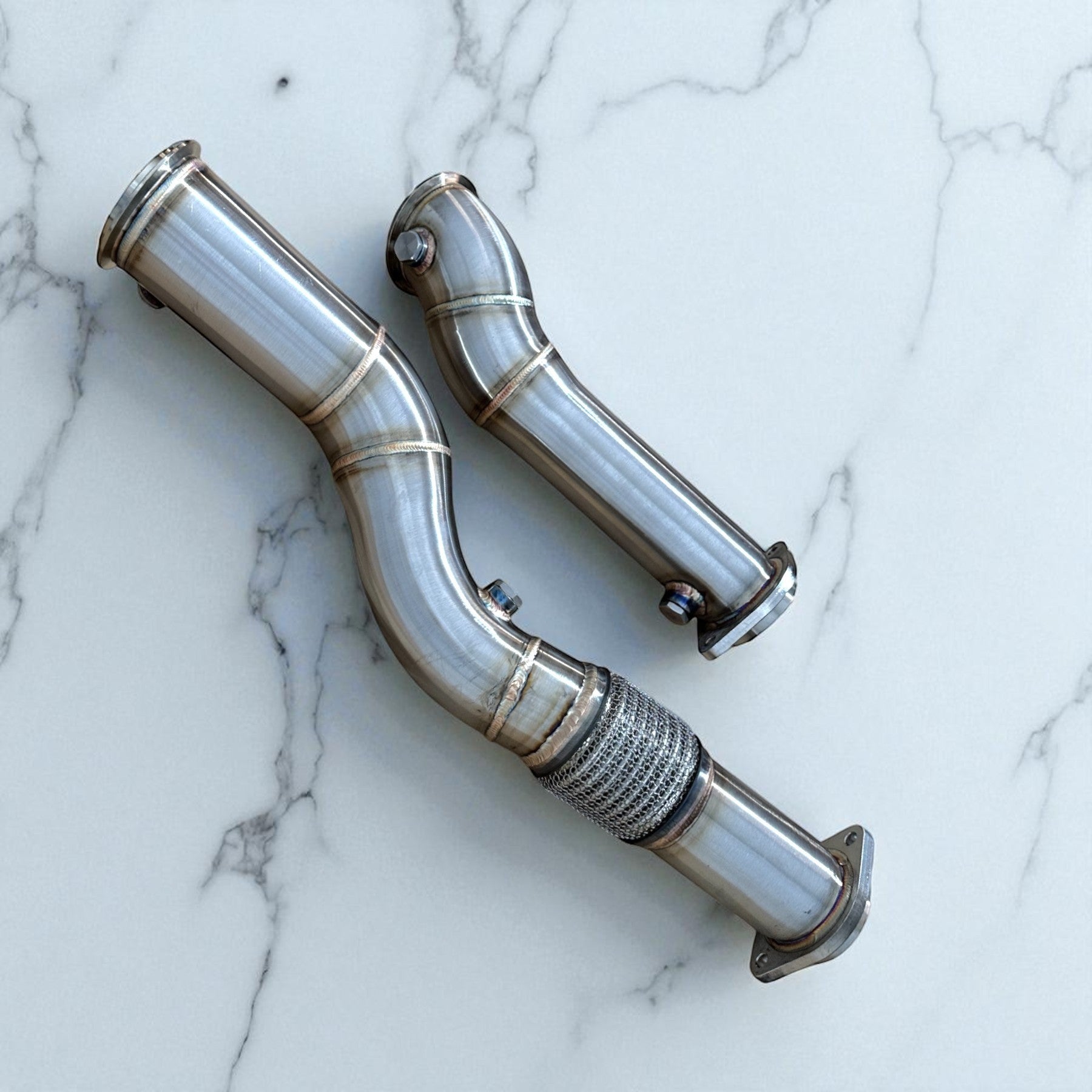Palenon Performance stainless steel catless race downpipes for BMW S58 engine on a white marble surface