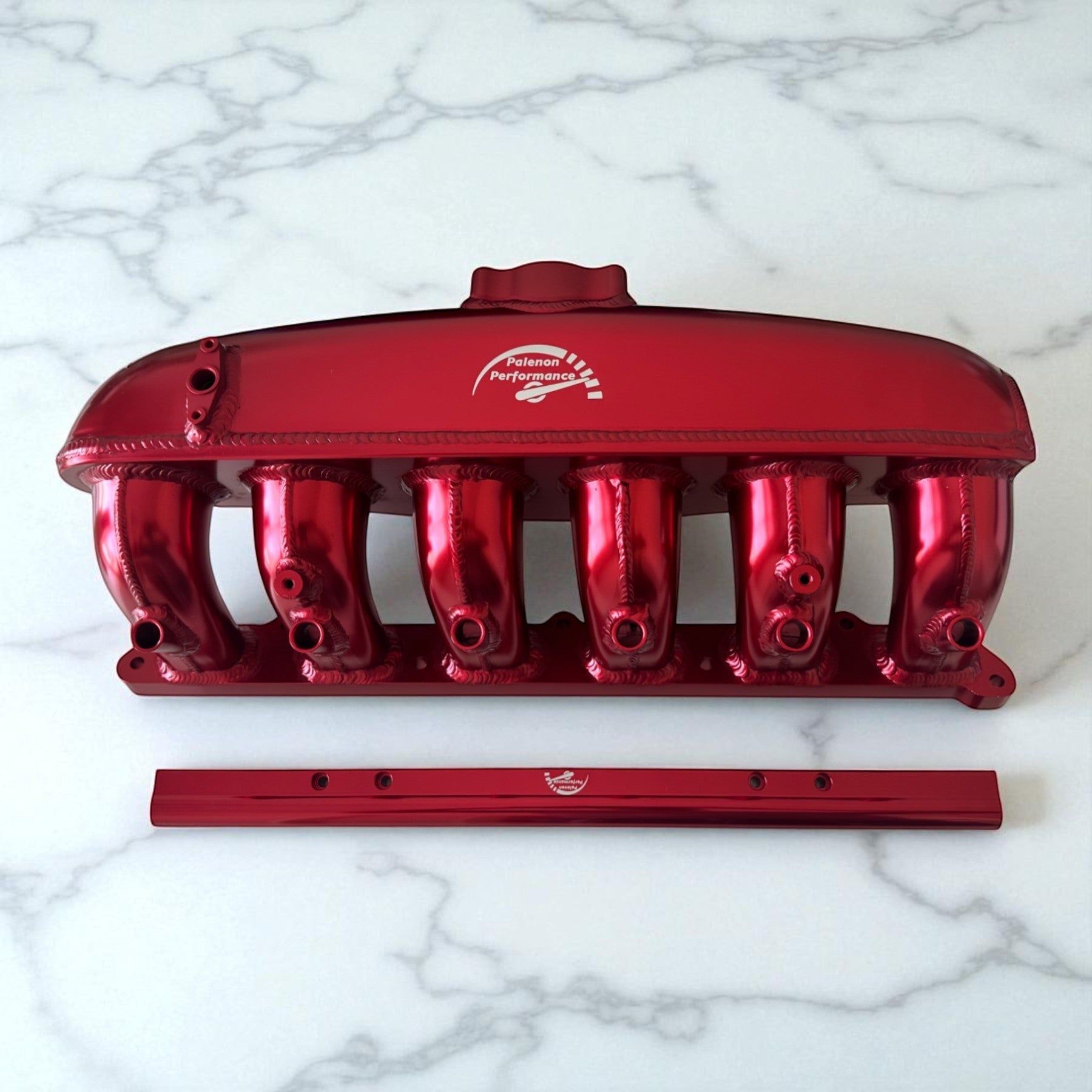 Palenon Performance red aluminum intake manifold with port injection rail for BMW N54 engines on white marble.